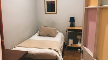 Un dormitorio pequeño y ordenado con una cama individual, una mesita de noche y una mesilla.