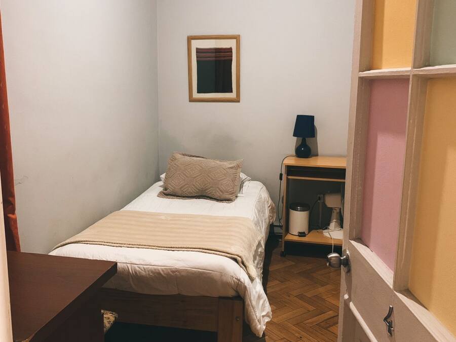 Un dormitorio pequeño y ordenado con una cama individual, una mesita de noche y una mesilla.