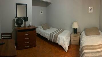 Un dormitorio con dos camas, televisión, cómoda, escritorio y lámpara.