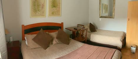 A room with two beds, a small table, chairs, a mirror, and two framed botanical illustrations on the wall.
