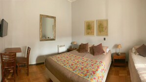 Un dormitorio con una cama grande, una cama más pequeña, un escritorio con silla, un espejo y dos lámparas de pared.