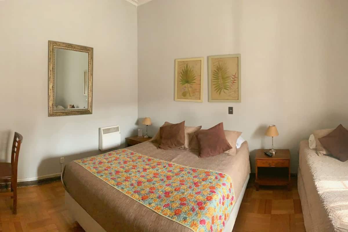 A bedroom with a large bed, a smaller bed, a desk with a chair, a mirror, and two wall-mounted lamps.