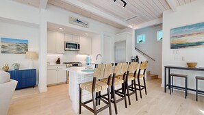 Une cuisine moderne avec des meubles blancs, un îlot central et un coin repas doté de chaises en osier.
