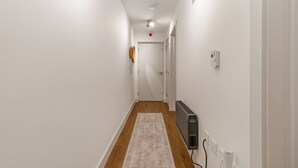 A narrow hallway with white walls, a wooden floor, and a light-colored rug. - Central 1BD Free Underground Parking (Cheltenham)