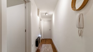 A narrow hallway with a wooden floor, white walls, a white door at the end, a wall-mounted telephone, and a ceiling light fixture. - Central 1BD Free Underground Parking (Cheltenham)