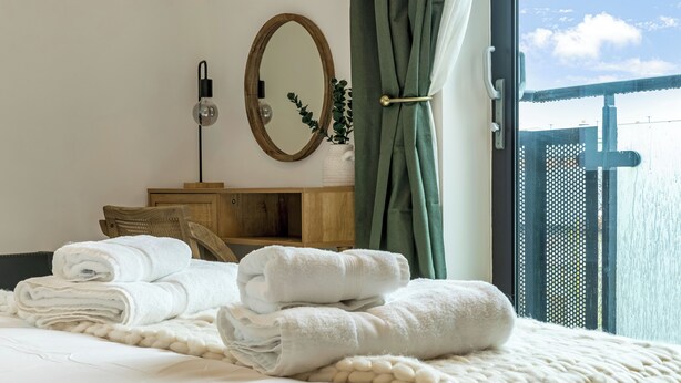 A hotel room with a bed, a wooden cabinet, a mirror, and a view of a balcony. - Central 1BD Free Underground Parking (Cheltenham)