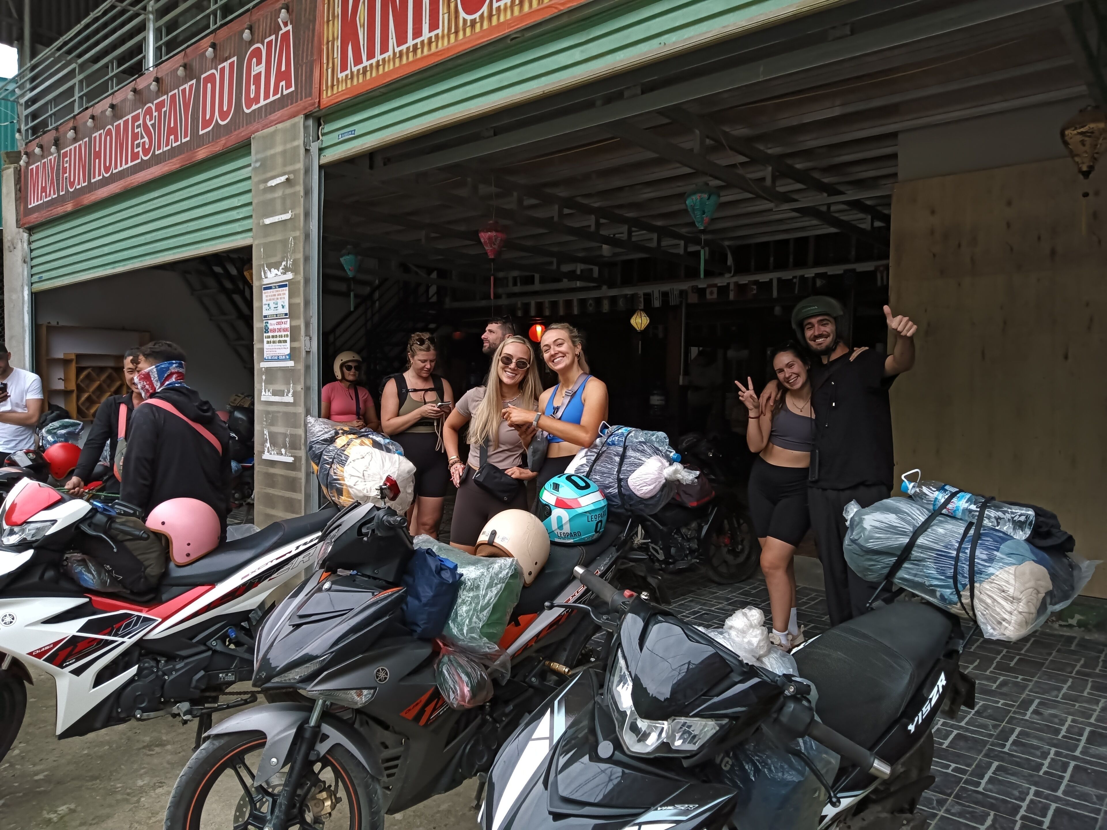 Un grupo de personas de pie frente a un edificio con un letrero que dice "MAX FUN HOMESTAY DU GIA".