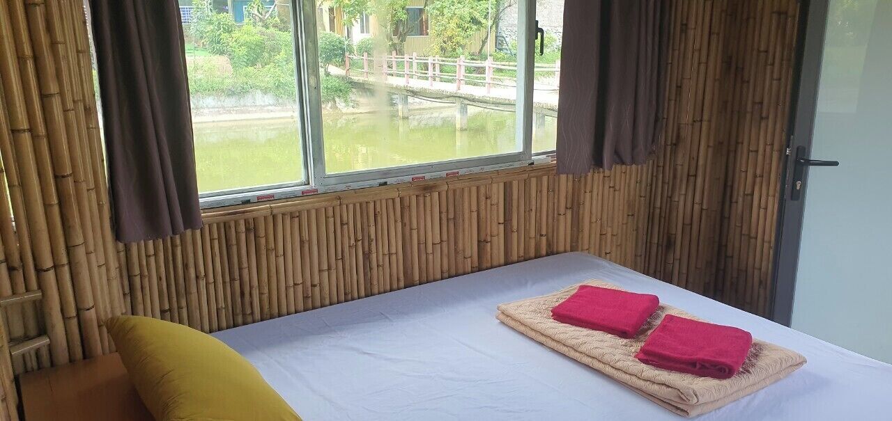 Een kamer met een bed, een raam met uitzicht op een waterpartij en een brug, en bamboe wandpanelen.