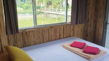 Een kamer met een bed, een raam met uitzicht op een waterpartij en een brug, en bamboe wandpanelen.