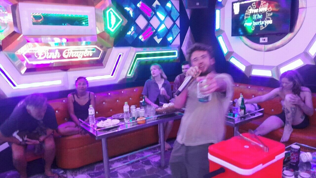 A brightly lit room with neon signs, a stage, and a group of people.