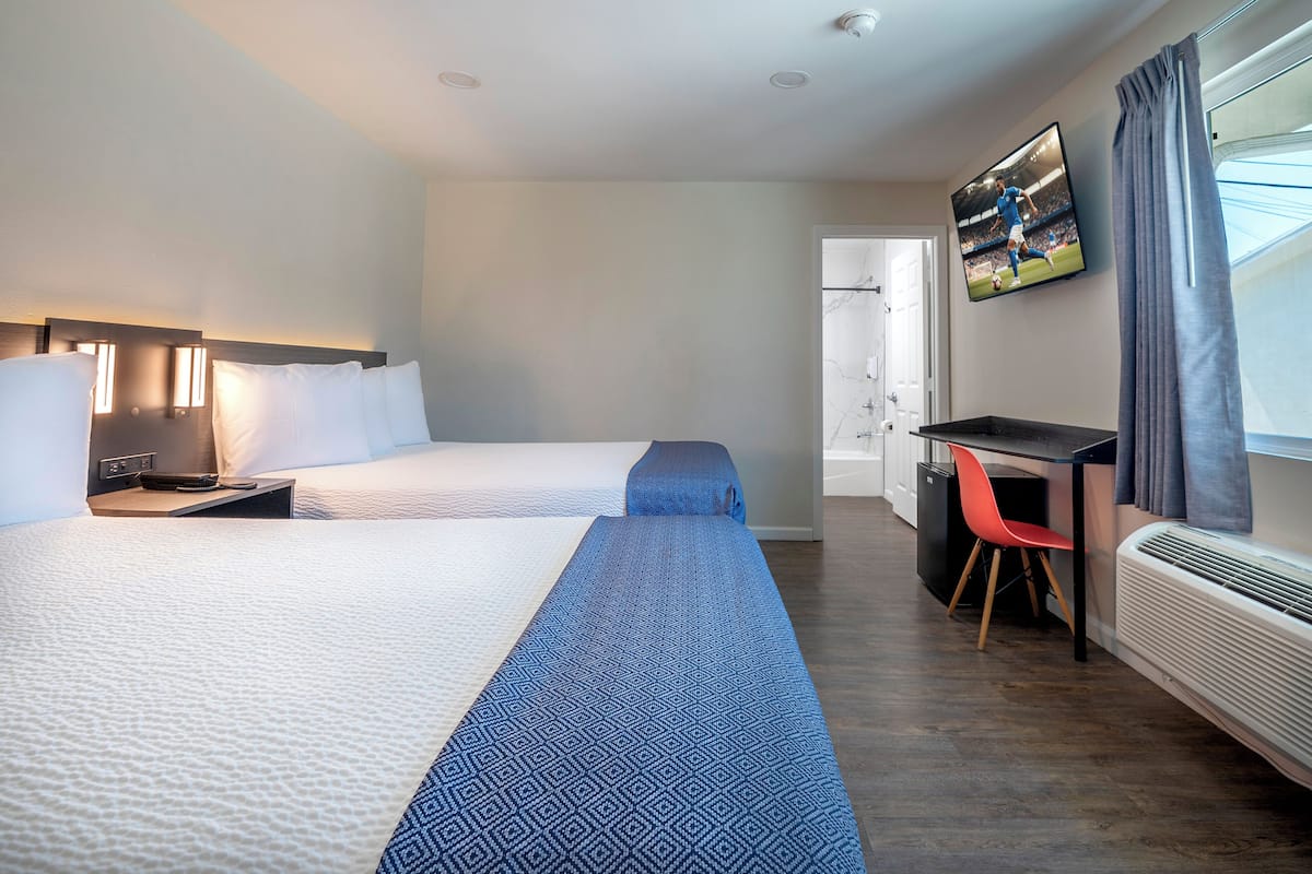 A hotel room with two beds, a desk, a chair, a television, and a window with curtains.