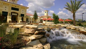 A hotel with a water feature in front, a clock tower, and palm trees.