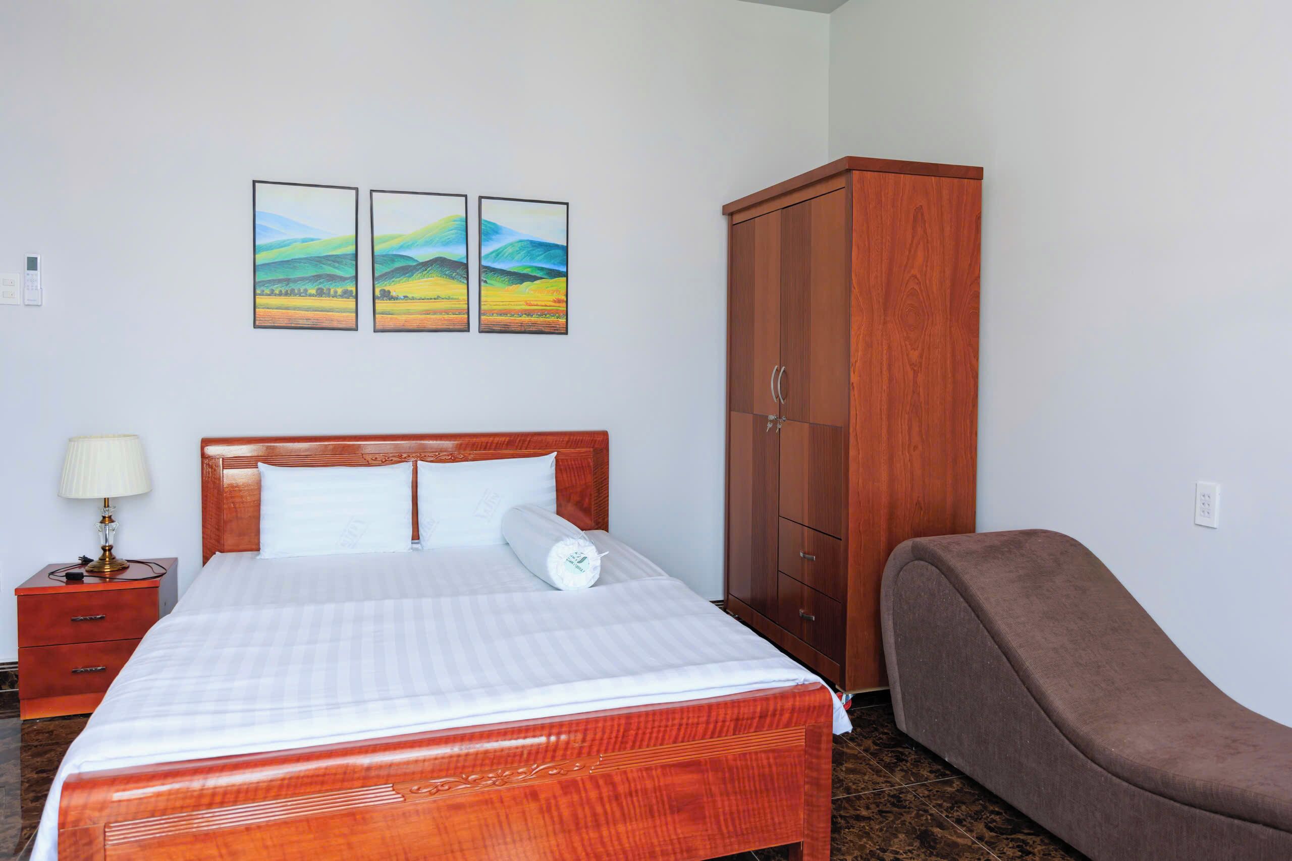 Ein Hotelzimmer mit einem hölzernen Bett, einem braunen Sessel, einem Kleiderschrank und zwei Landschaftsbildern an der Wand.