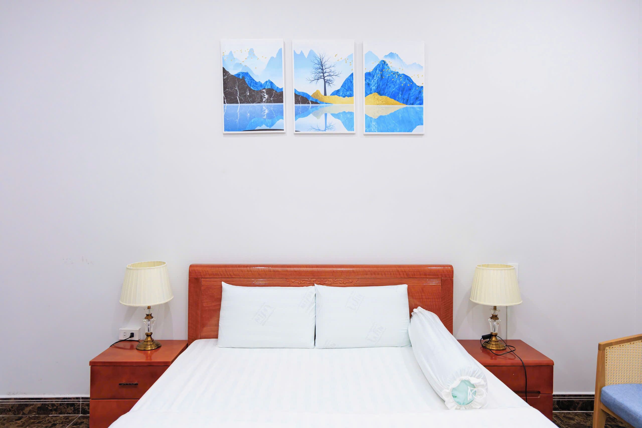 A hotel room with a wooden bed, two bedside tables with lamps, and three paintings on the wall.