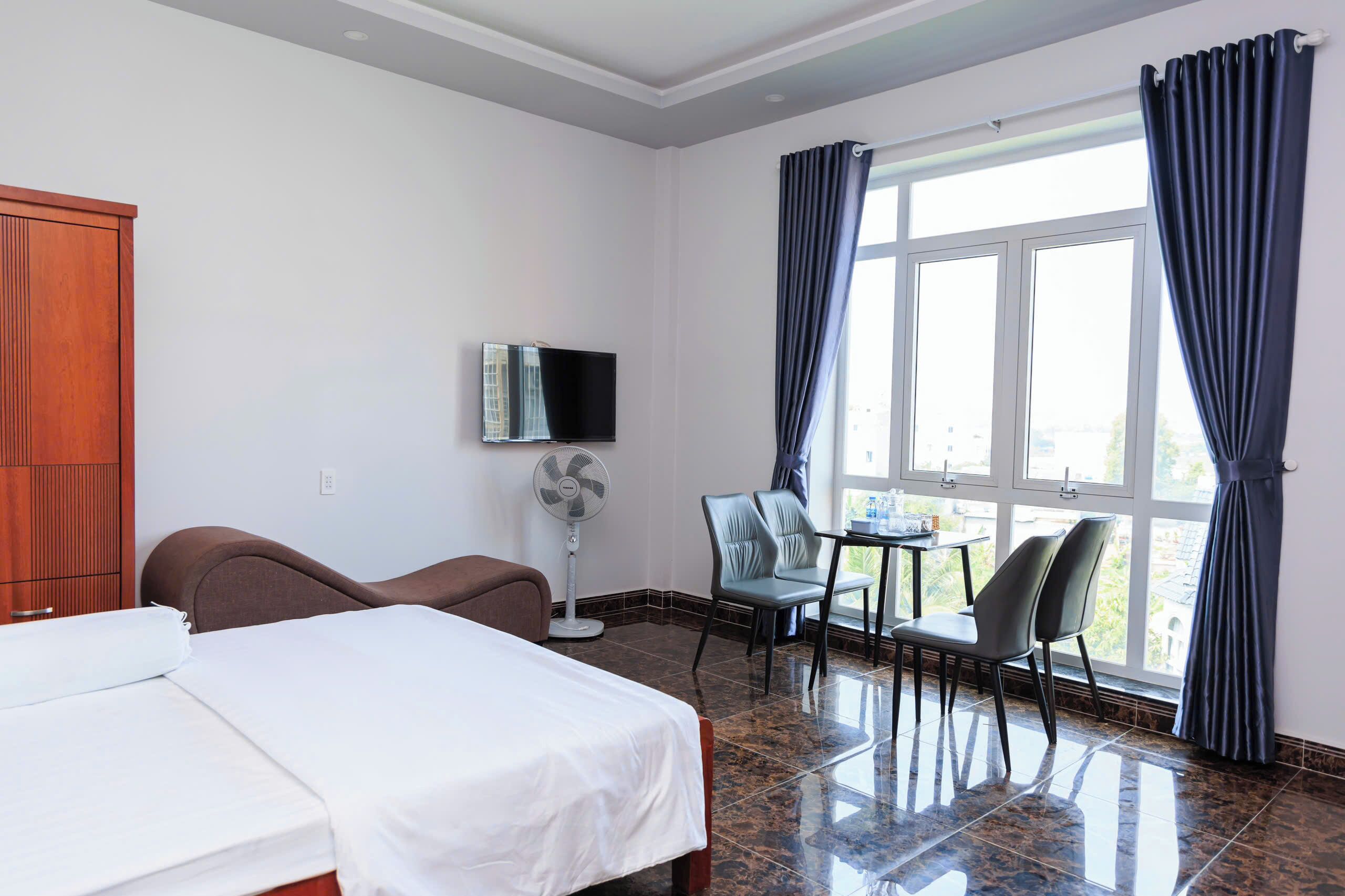 A hotel room with a bed, a desk with two chairs, a TV, and a window with curtains.