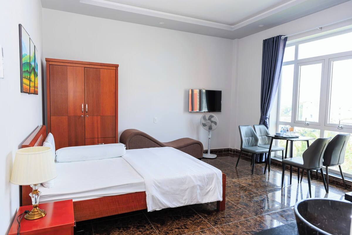 Une chambre d’hôtel avec un lit, un bureau, une chaise, une télévision et une fenêtre avec des rideaux.