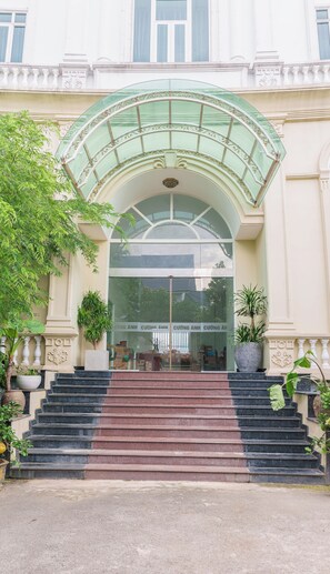 Una imponente entrada con puerta de vidrio, un arco de vidrio verde y una escalera que sube hacia la entrada.