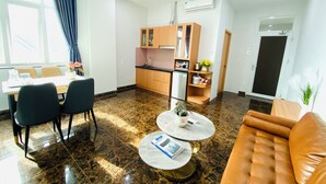 A modern living room with a brown leather sofa, a dining area with a table and chairs, a kitchen with wooden cabinets, and a large window with curtains. - Cuong Anh House (Ho Chi Minh City)