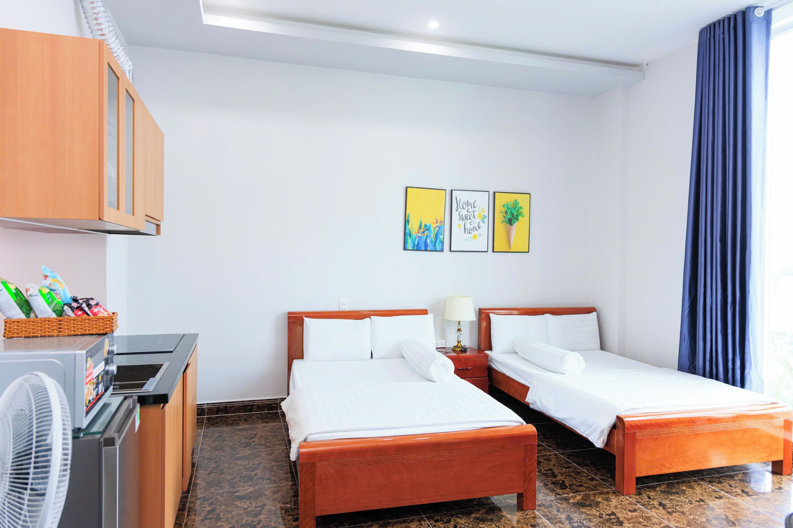 Une chambre d’hôtel avec deux lits, une armoire en bois, un ventilateur et une petite table avec une lampe.