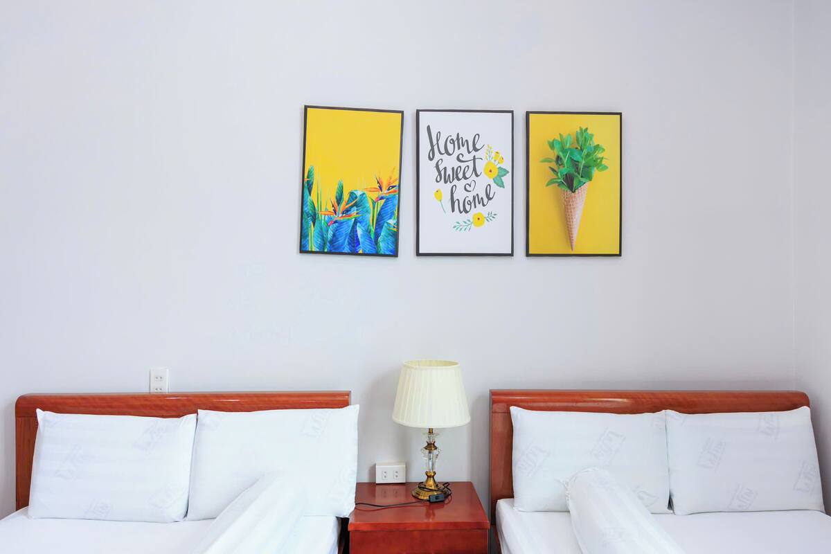 Une chambre d’hôtel avec deux lits, une table de chevet avec une lampe et trois œuvres d’art encadrées accrochées au mur.