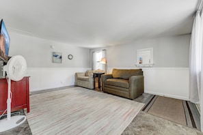 A living room with a red cabinet, a white fan, two sofas, a rug, and a small table with a lamp. - The Barracks (Colorado Springs)