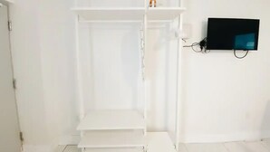 A white room with a built-in shelving unit, a flat-screen TV mounted on the wall, and a door on the left. - Studio | 2 Beds |  Kitchen | Rooftop| Near Beach (Miami beach)