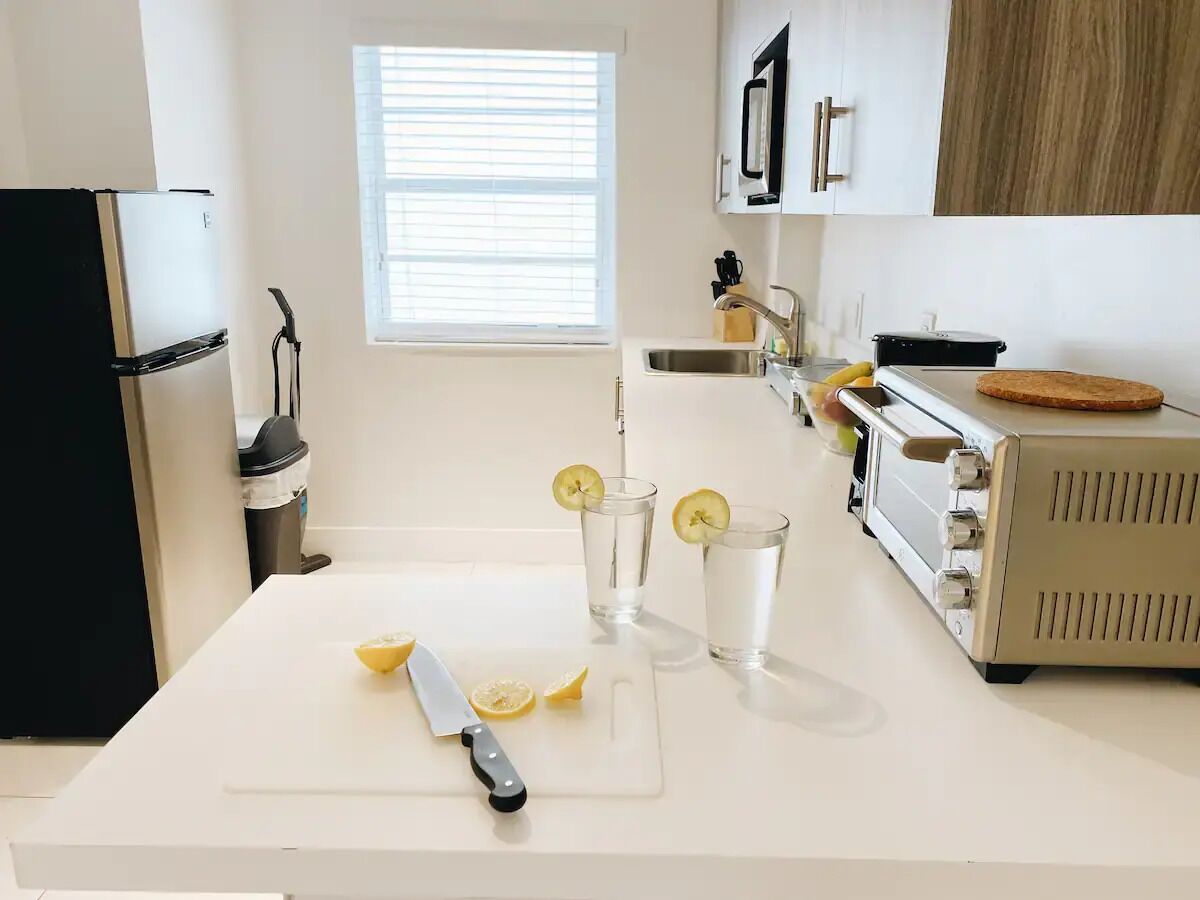 A kitchen with a white countertop, a black refrigerator, a toaster, and a window with blinds.