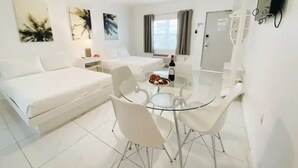 A modern, white-themed room with a bed, a dining table with chairs, a TV mounted on the wall, and artwork on the walls. - Studio | 2 Beds |  Kitchen | Rooftop| Near Beach (Miami beach)