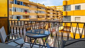 Ein Balkon mit Glastisch und Stühlen, mit Blick auf ein gelbes Gebäude mit mehreren Balkonen und Klimaanlagen.