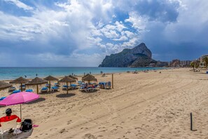 A beach with umbrellas, lounge chairs, and a mountain in the background.