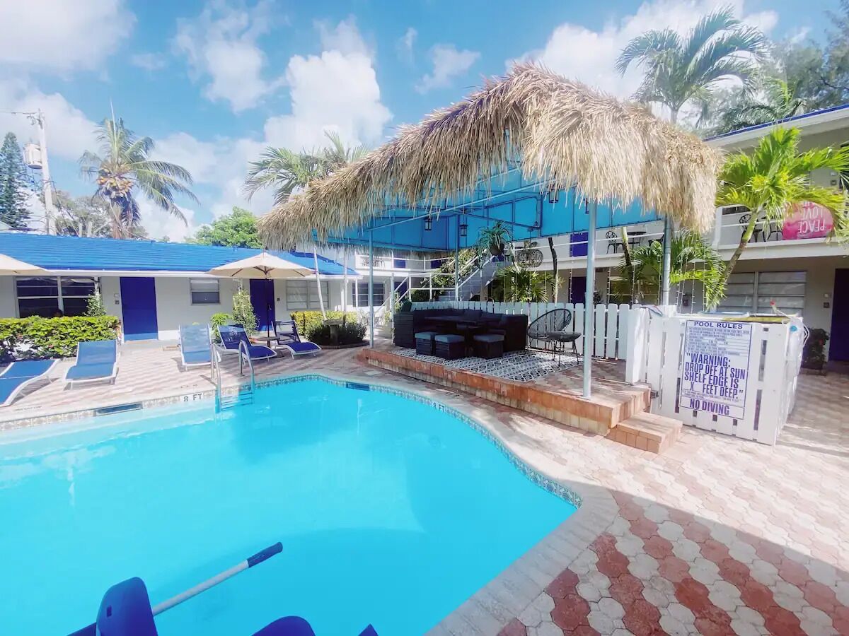 Une piscine avec des chaises longues, une structure dotée d’un toit de chaume et un panneau indiquant les règles à respecter au bord de la piscine.