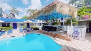 Una piscina con sillas de descanso, una estructura de techo de paja y un cartel con las normas de la piscina.
