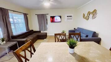 A living room with a sofa, a TV, a ceiling fan, and a dining table with chairs.