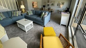 A living room with a sofa, ottoman, coffee table, and a dining area with chairs and a table.