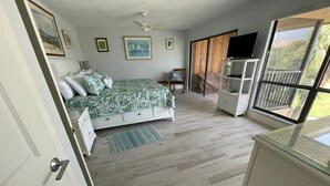 A bedroom with a bed, a TV, a desk, and a balcony with a view.
