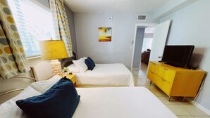 A hotel room with two beds, a TV, a yellow dresser, and a painting on the wall. - Spacious 1 Bedroom Double Apt - Pool, Free Parking, Walk to Beach! (Lauderdale by the sea)