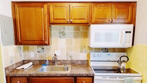 Una cocina con gabinetes de madera, encimera de granito, un fregadero, una estufa y un microondas.
