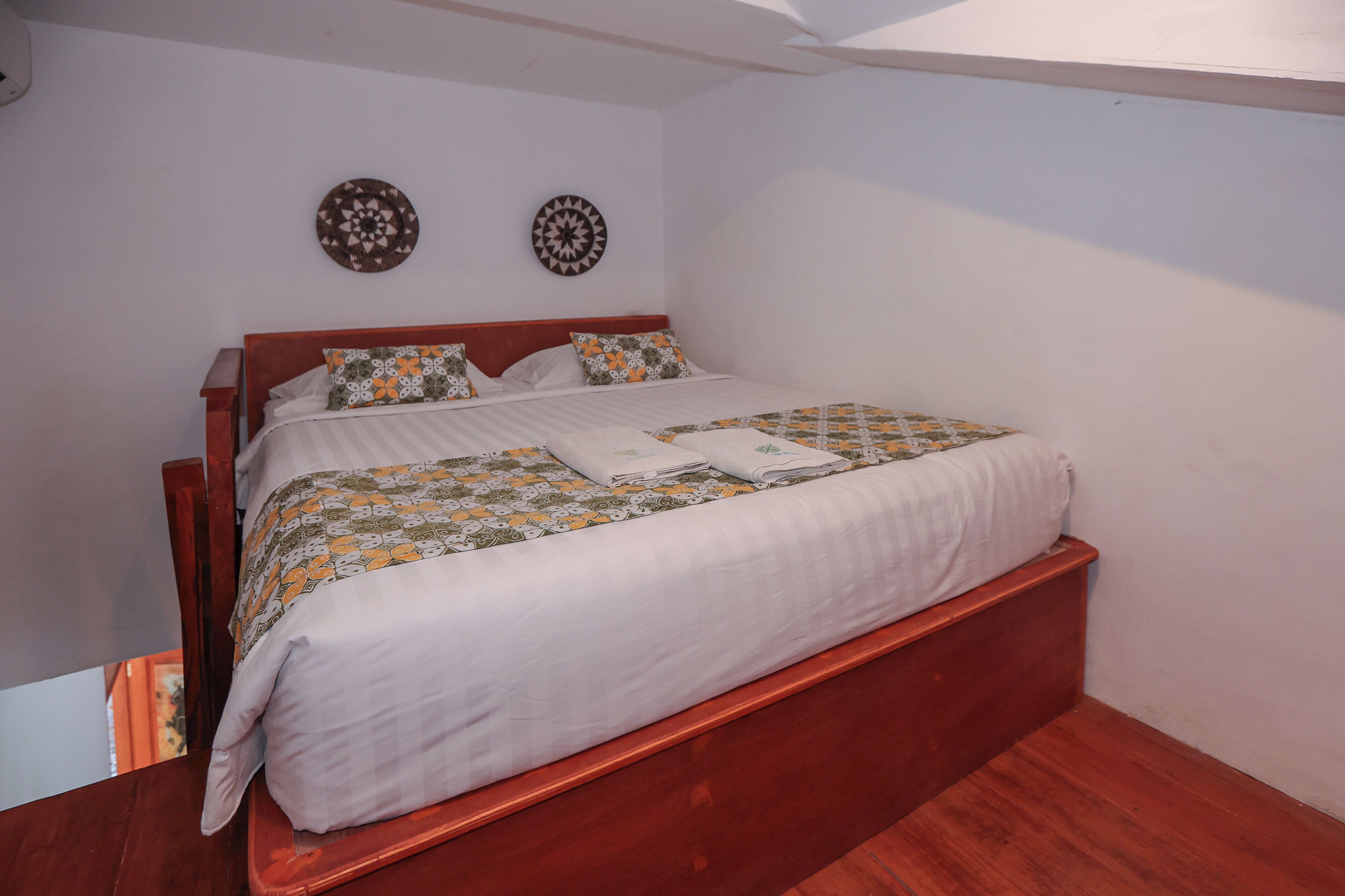 A neatly made bed with patterned bedding, a wooden headboard, and two wall decorations.