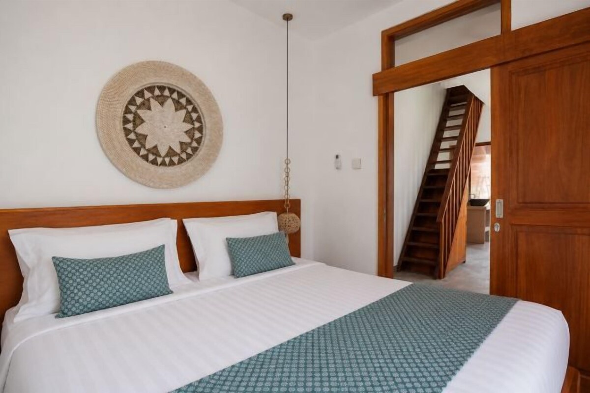 A bedroom with a bed, two pillows, a wall hanging, and a wooden door.