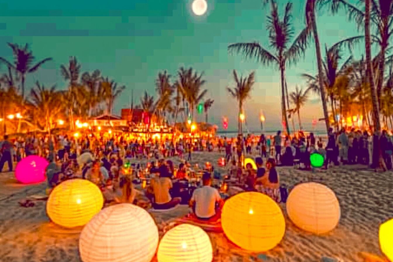A beach scene with palm trees and people gathered around.