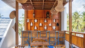 Un espace extérieur aménagé avec des meubles en bois, comprenant des tables et des chaises, une statue de Bouddha et des étagères ornées de divers objets décoratifs.