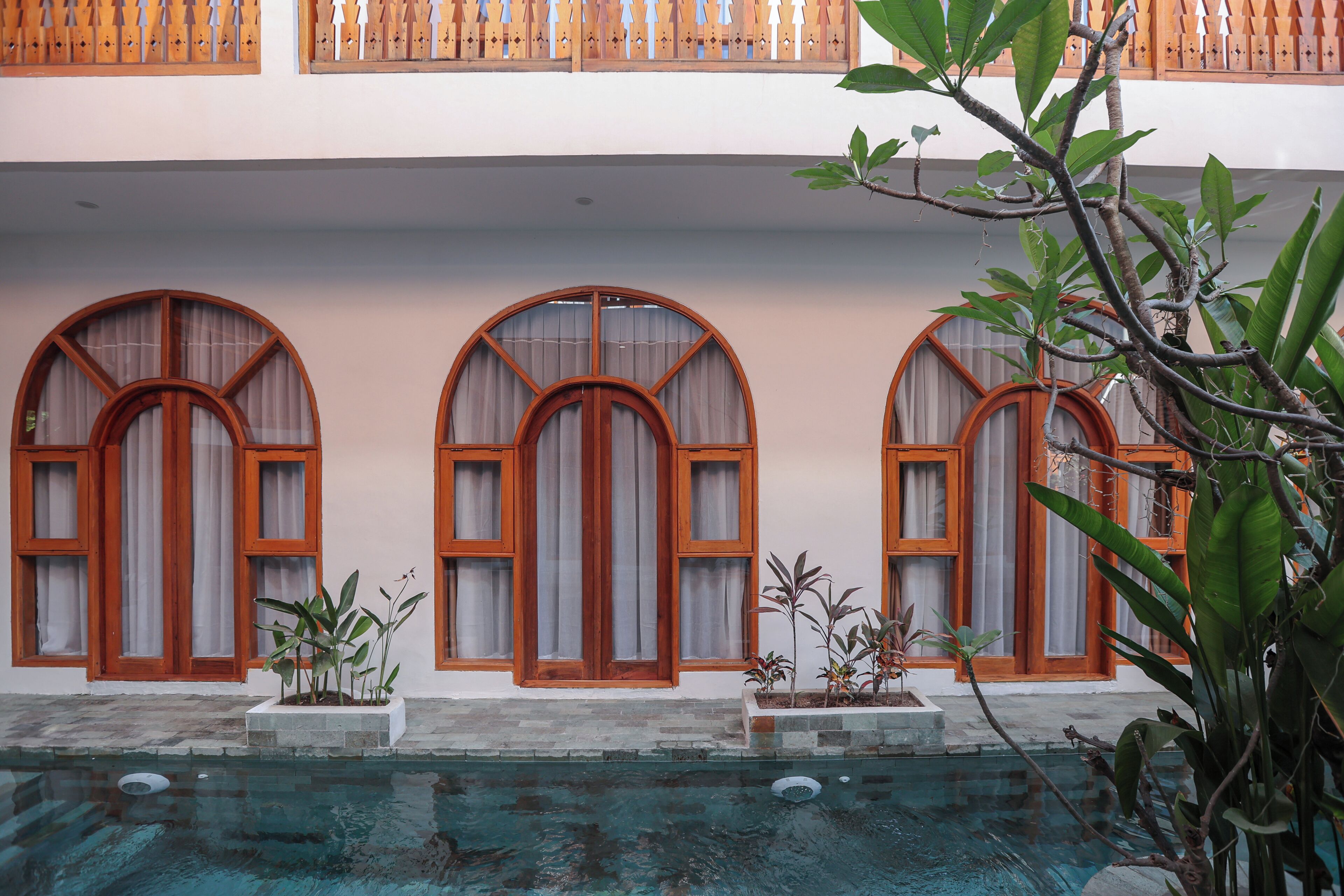 A pool with arched windows and wooden railings, surrounded by potted plants.