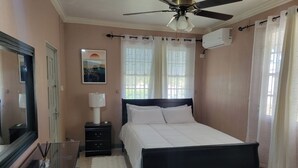 A bedroom with a bed, a nightstand, a lamp, a ceiling fan, and a window with curtains.