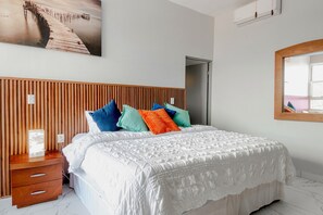 Un dormitorio ordenado con cabecera de madera, cubrecama blanco y almohadas coloridas.