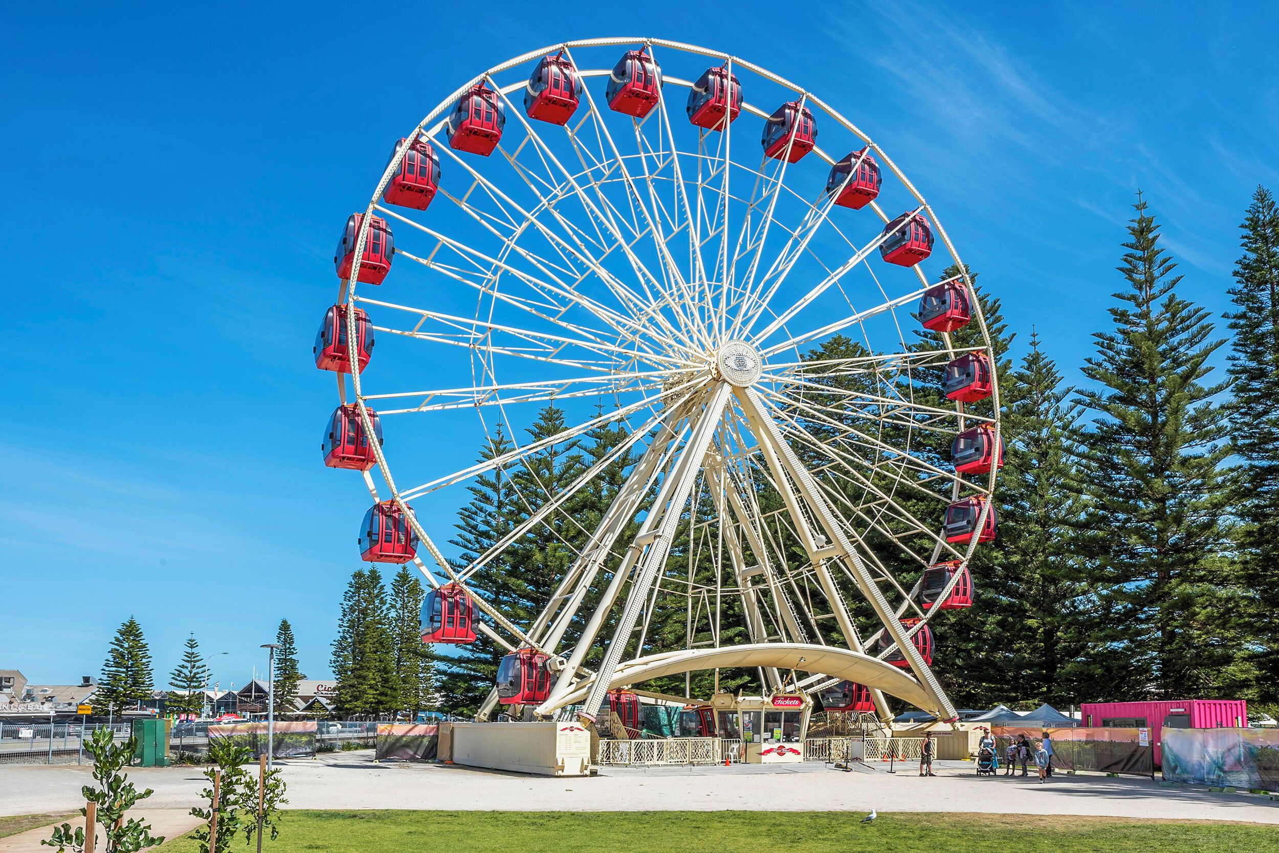 A large Ferris wheel with red gondolas, surrounded by trees and a clear sky.