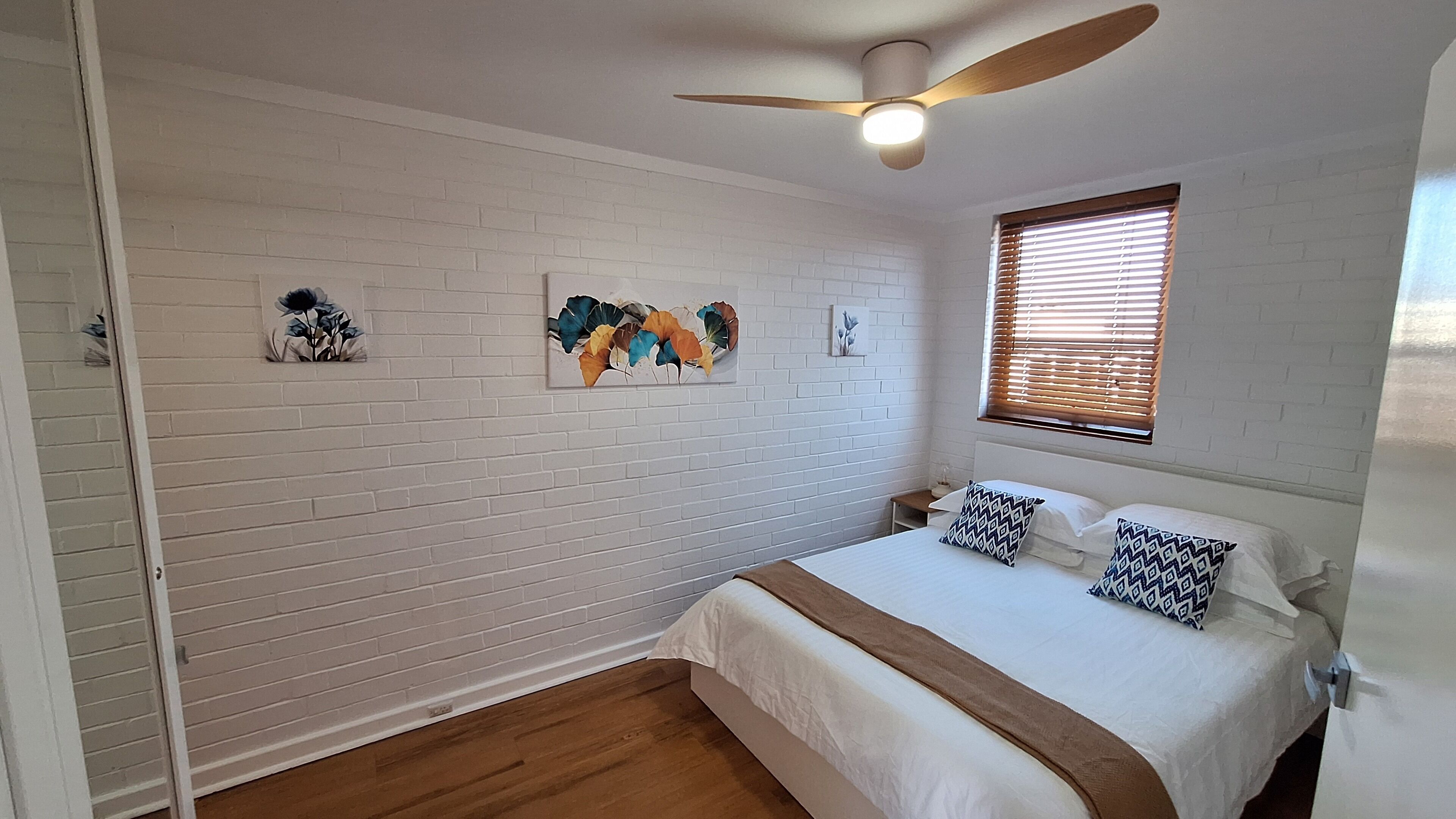 A bedroom with a bed, a ceiling fan, a window with blinds, and artwork on the wall.