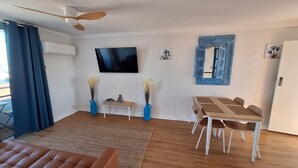 Un salon moderne avec un téléviseur à écran plat, une table à manger avec des chaises, un canapé et des vases décoratifs.
