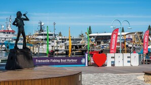 Une statue représentant une femme tenant un microphone, un panneau indiquant le port de pêche de Fremantle, et un grand panneau rouge en forme de cœur sur lequel est inscrit le mot « FREO ».