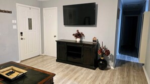 Una sala de estar con un mueble de centro de entretenimiento de madera oscura, un televisor de pantalla plana montado en la pared y una mesa de centro de madera con un control remoto.