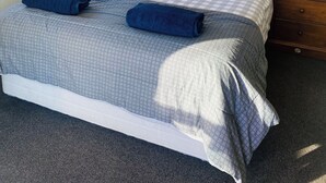 Un lit bien fait, avec une couverture à carreaux, deux oreillers et deux serviettes enroulées.